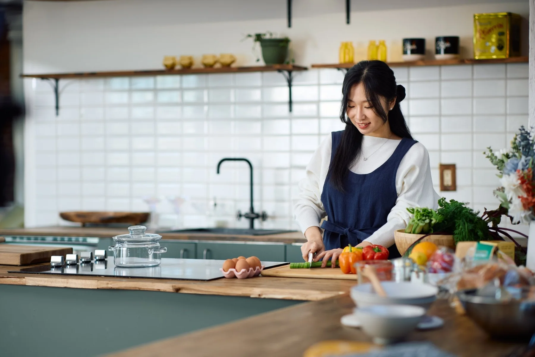 Preparing fresh vegetables in a sunlit kitchen, wearing Hanee's navy linen pinafore apron